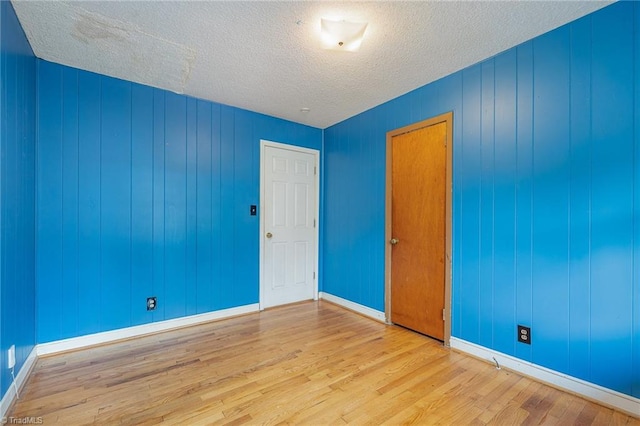 empty room featuring a textured ceiling, wooden walls, and light hardwood / wood-style flooring