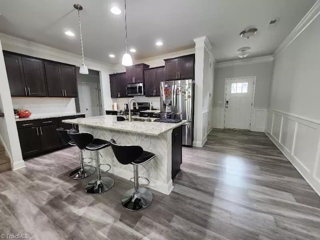 kitchen featuring appliances with stainless steel finishes, a breakfast bar, ornamental molding, dark brown cabinetry, and a center island with sink