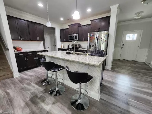 kitchen with sink, appliances with stainless steel finishes, dark brown cabinetry, an island with sink, and decorative light fixtures