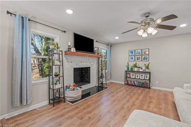 living room featuring a brick fireplace, a wealth of natural light, ceiling fan, and light wood-type flooring