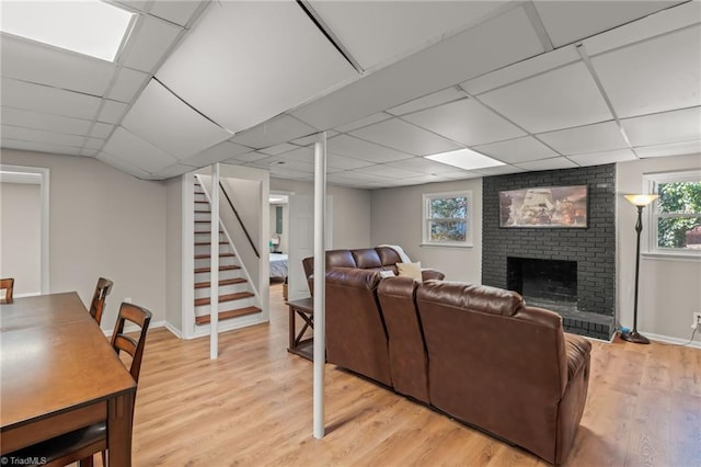 living room with a drop ceiling, a fireplace, and light hardwood / wood-style floors