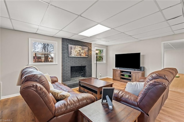 living room with light hardwood / wood-style floors, a brick fireplace, and a drop ceiling