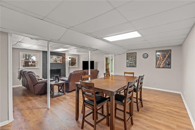 dining area featuring a brick fireplace, a paneled ceiling, and light hardwood / wood-style flooring