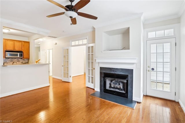 unfurnished living room with ceiling fan, ornamental molding, and light wood-type flooring