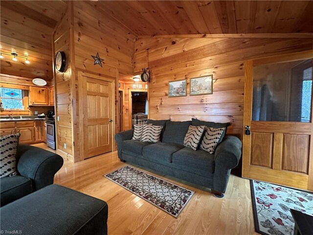 living room featuring sink, light hardwood / wood-style flooring, wooden ceiling, lofted ceiling, and wood walls