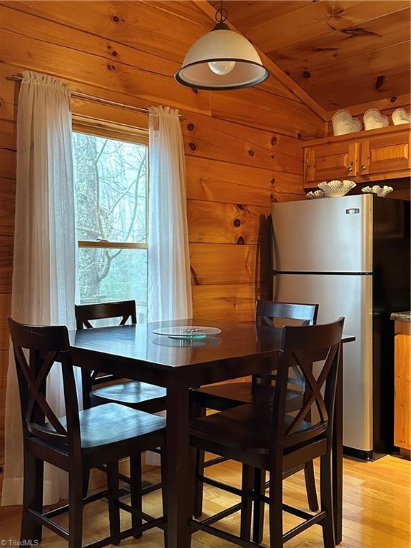 dining room featuring wood walls, wood ceiling, light hardwood / wood-style flooring, and vaulted ceiling