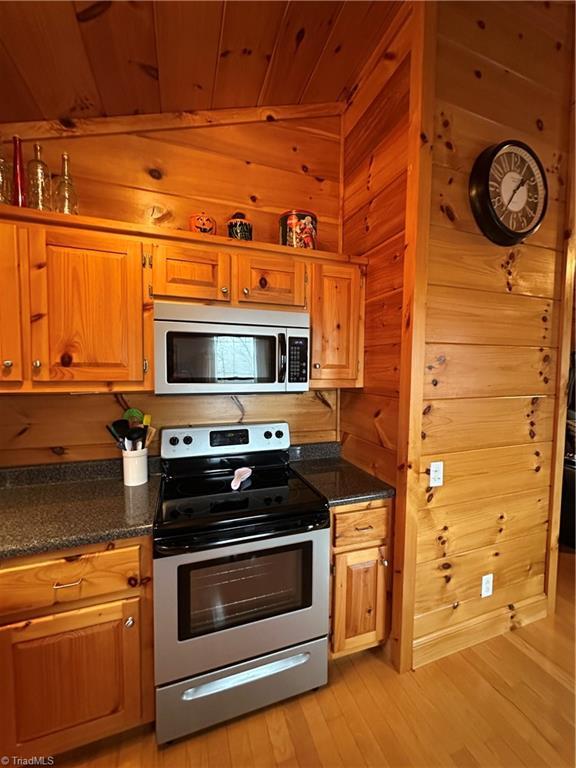 kitchen with dark stone counters, wood walls, and stainless steel appliances