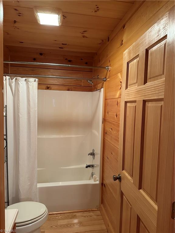 bathroom with hardwood / wood-style flooring, shower / bathtub combination with curtain, wooden ceiling, toilet, and wood walls