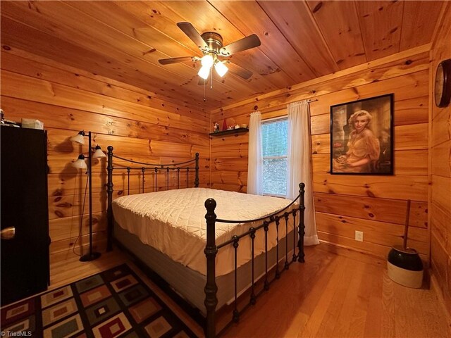 bedroom with ceiling fan, wood-type flooring, wooden ceiling, and wooden walls