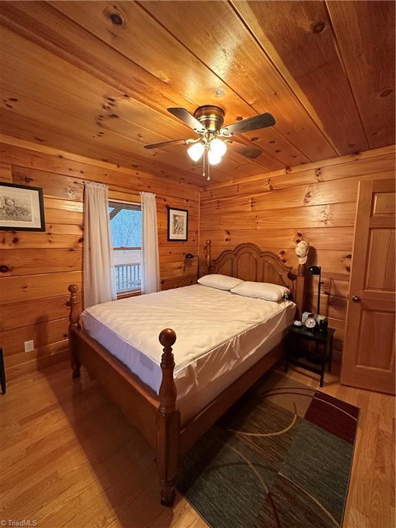 bedroom featuring ceiling fan, light hardwood / wood-style flooring, wooden ceiling, and wood walls