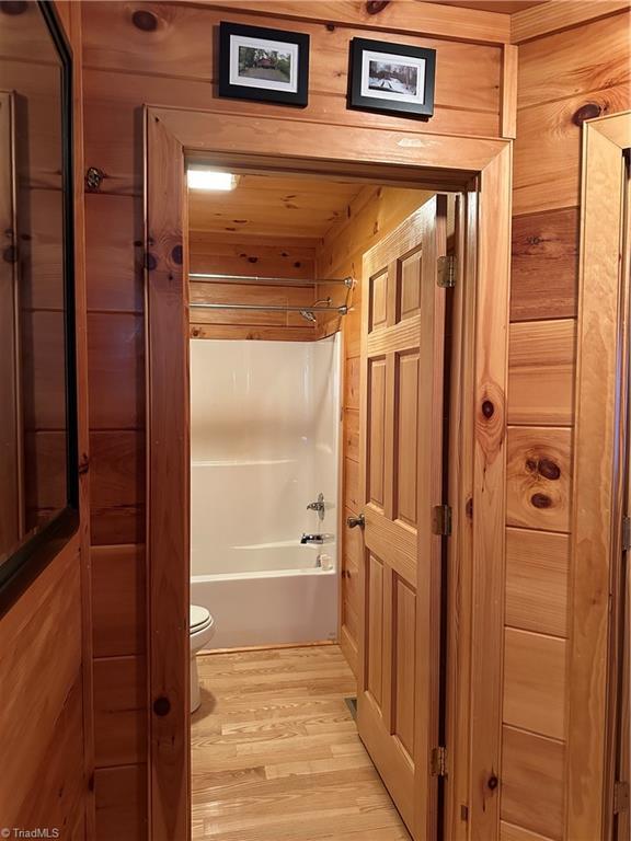 bathroom with hardwood / wood-style floors, toilet, shower / tub combination, and wood walls