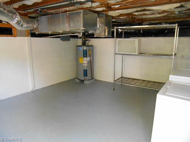 unfinished below grade area featuring electric water heater, concrete block wall, and washing machine and clothes dryer