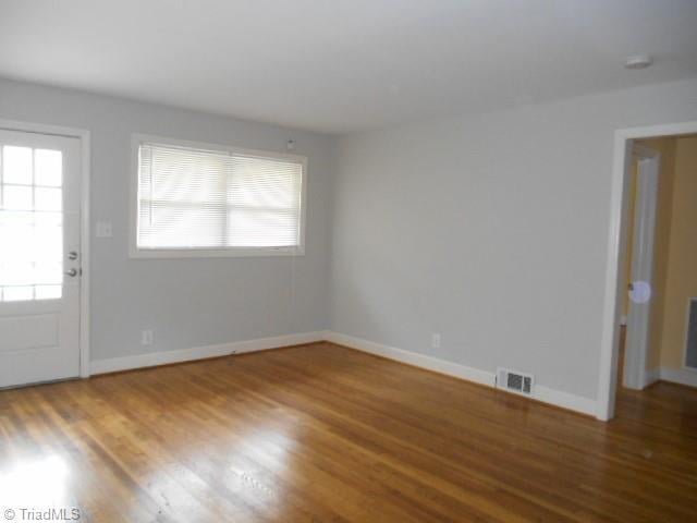 spare room with wood finished floors, visible vents, and baseboards