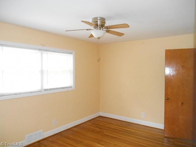 empty room with wood finished floors, baseboards, visible vents, and ceiling fan