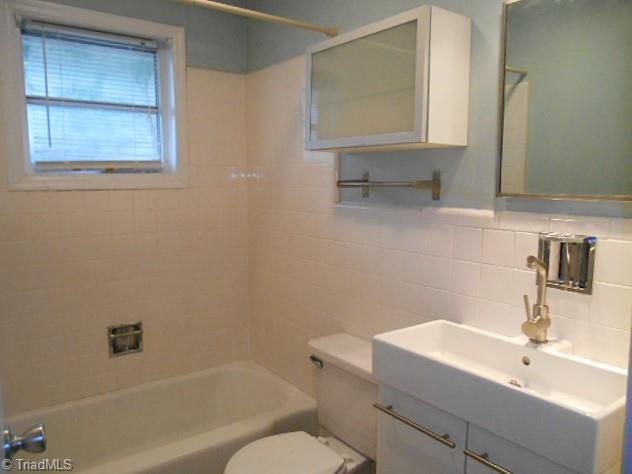 full bath featuring shower / bath combination, vanity, toilet, and tile walls