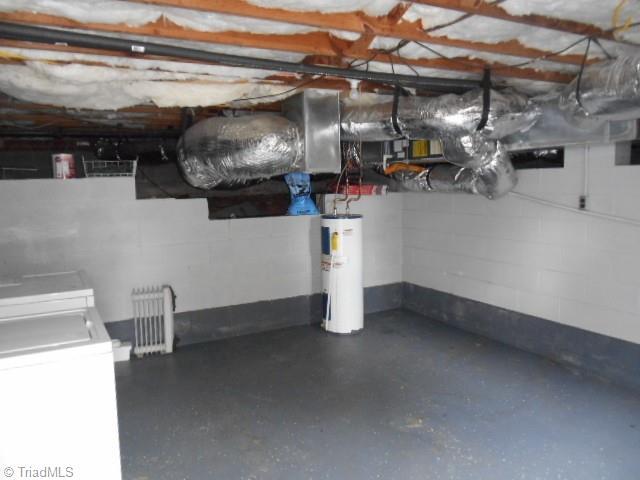 basement featuring water heater, concrete block wall, and radiator heating unit