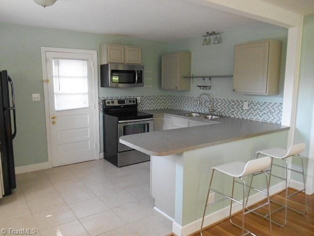 kitchen featuring backsplash, a breakfast bar area, a peninsula, stainless steel appliances, and a sink