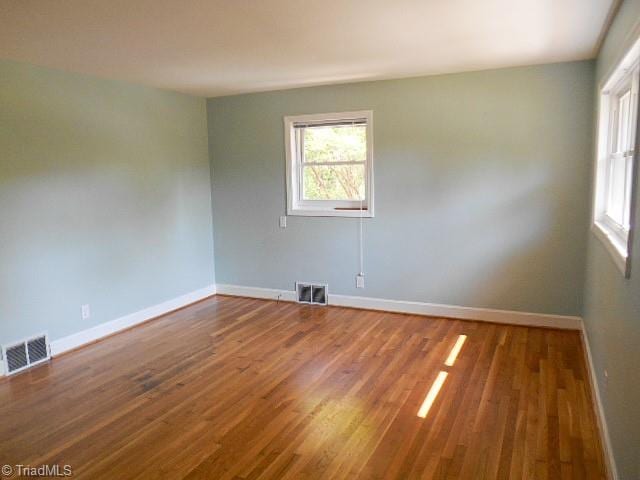 empty room with wood finished floors, visible vents, and baseboards