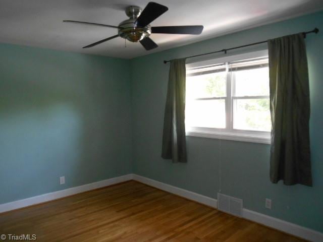 empty room with a ceiling fan, visible vents, wood finished floors, and baseboards