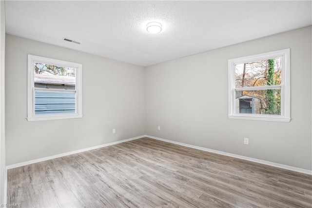 unfurnished room with light wood-type flooring and a textured ceiling