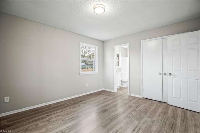 unfurnished bedroom with wood-type flooring, a textured ceiling, ensuite bathroom, and a closet