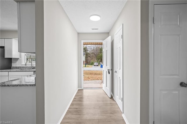 corridor with sink, a textured ceiling, and light wood-type flooring