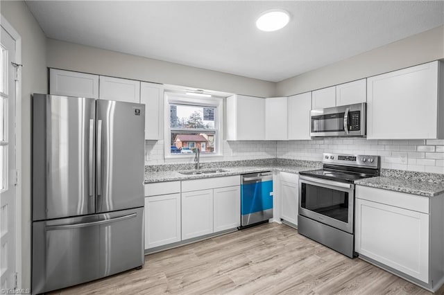 kitchen with light stone countertops, stainless steel appliances, sink, white cabinets, and light hardwood / wood-style floors