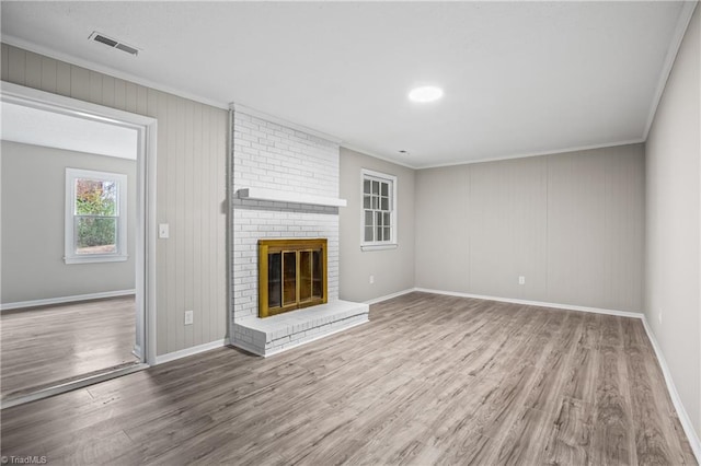 unfurnished living room featuring a brick fireplace, ornamental molding, and hardwood / wood-style flooring