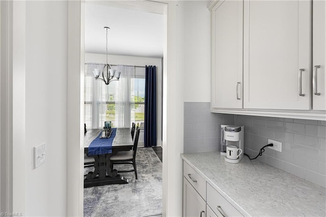 kitchen featuring a chandelier, decorative backsplash, light stone countertops, and white cabinetry
