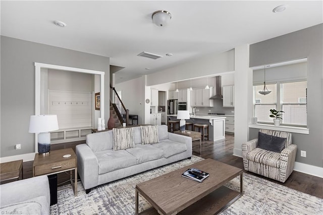 living room with dark wood-style flooring, baseboards, and stairs