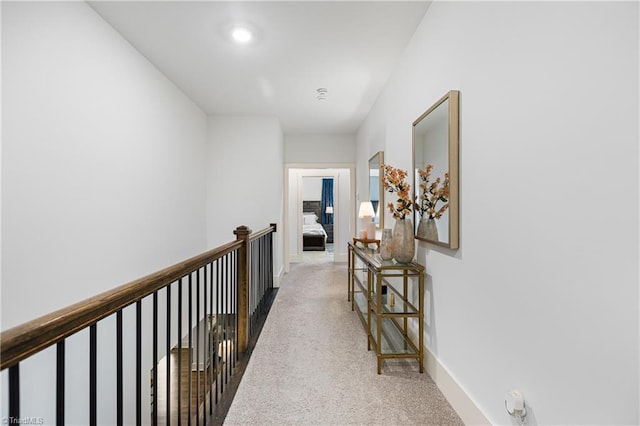 hall with carpet flooring, baseboards, and an upstairs landing