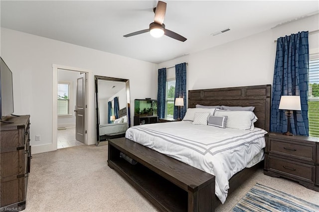 bedroom featuring light colored carpet, a ceiling fan, ensuite bathroom, and baseboards