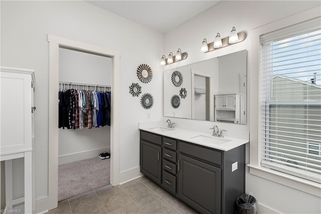 bathroom with double vanity, a walk in closet, baseboards, and tile patterned floors