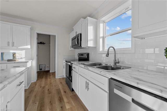 kitchen with light wood finished floors, decorative backsplash, appliances with stainless steel finishes, white cabinets, and a sink