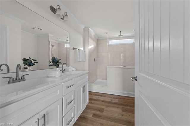 full bath featuring a tile shower, ornamental molding, and a sink