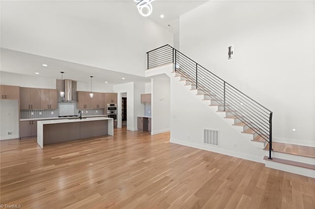 unfurnished living room with sink, light hardwood / wood-style flooring, and a high ceiling