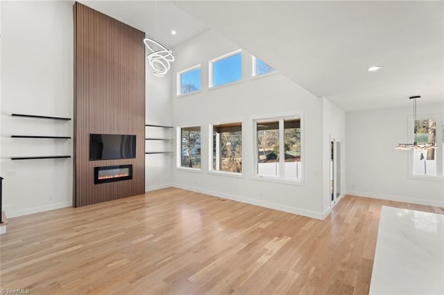 unfurnished living room featuring a fireplace, light hardwood / wood-style floors, a high ceiling, and a notable chandelier