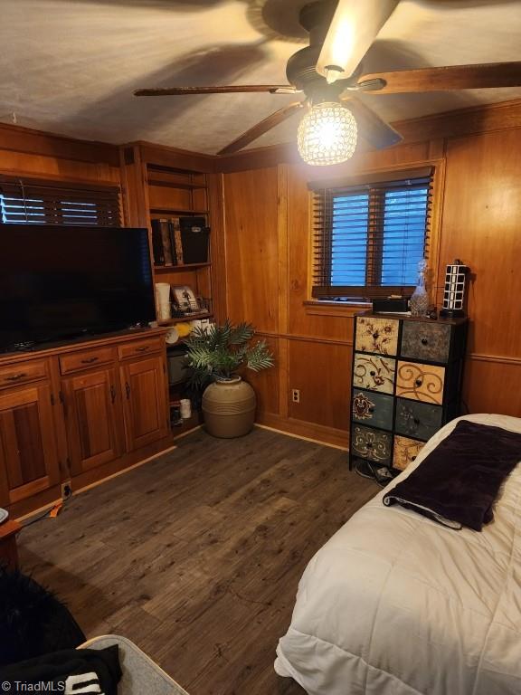 bedroom with dark hardwood / wood-style flooring, wood walls, and ceiling fan