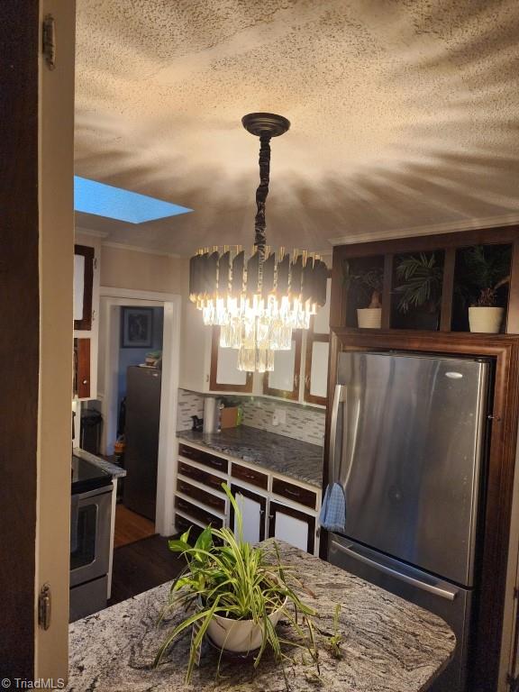 kitchen with appliances with stainless steel finishes, a textured ceiling, decorative backsplash, dark wood-type flooring, and a skylight