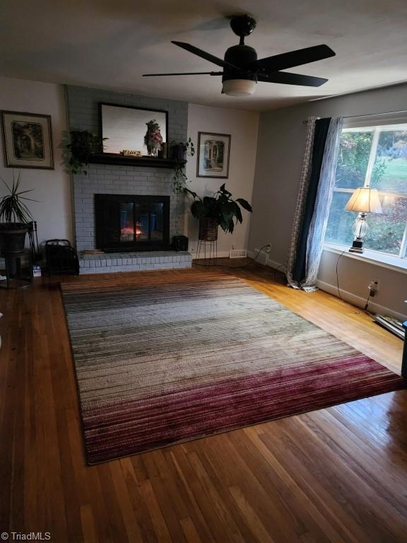 living room with ceiling fan, a brick fireplace, and light hardwood / wood-style flooring