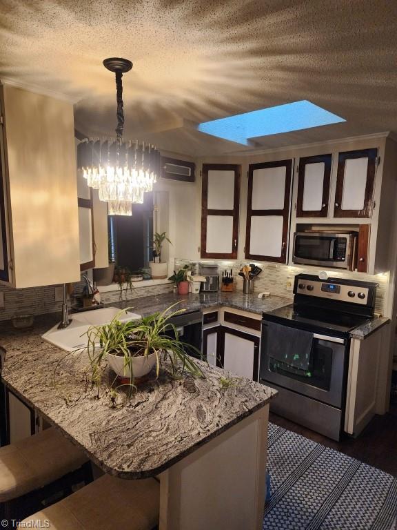 kitchen with stainless steel appliances, kitchen peninsula, a textured ceiling, a skylight, and hanging light fixtures