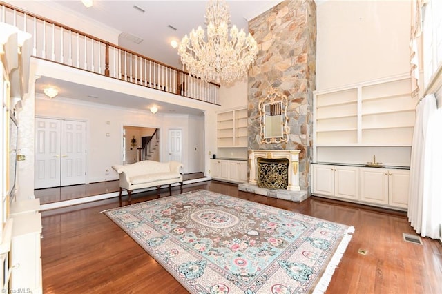 living room with a stone fireplace, a chandelier, built in features, and dark hardwood / wood-style flooring