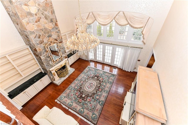 living room with an inviting chandelier, a high ceiling, a fireplace, dark hardwood / wood-style flooring, and french doors