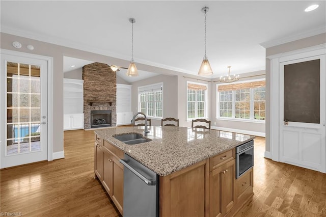 kitchen with a fireplace, hanging light fixtures, light wood-style flooring, a sink, and dishwasher