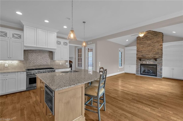 kitchen featuring light stone counters, stainless steel range, a sink, a stone fireplace, and light wood-type flooring