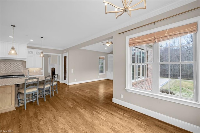 kitchen featuring light stone counters, wood finished floors, white cabinetry, baseboards, and decorative backsplash