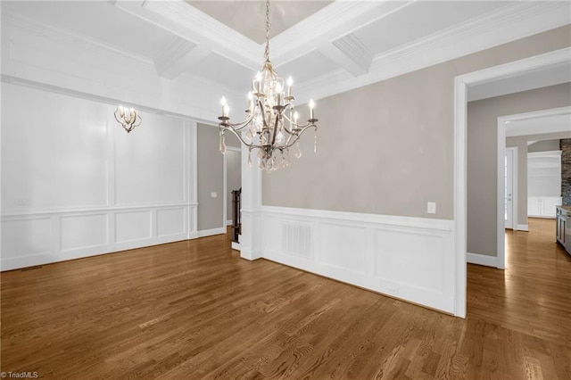 unfurnished dining area with beamed ceiling, coffered ceiling, wood finished floors, and a decorative wall