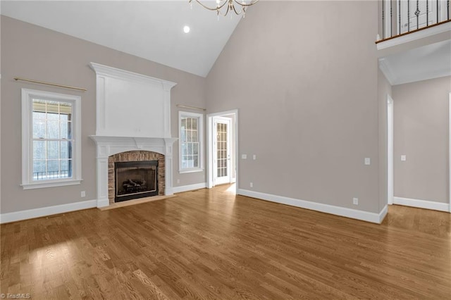 unfurnished living room featuring light wood-style floors, baseboards, a brick fireplace, and high vaulted ceiling