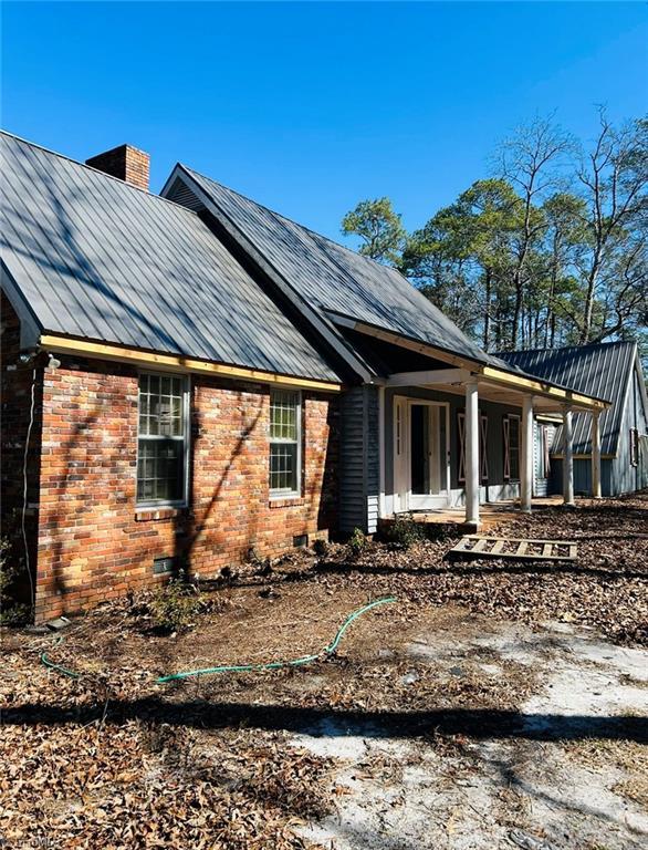 view of home's exterior featuring crawl space, a chimney, metal roof, and brick siding