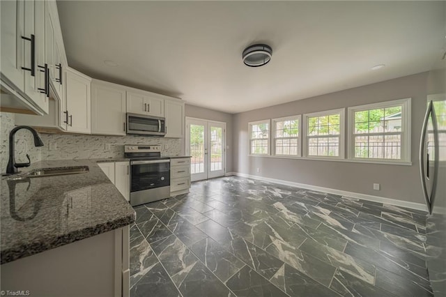 kitchen with stainless steel appliances, white cabinetry, sink, and dark stone counters